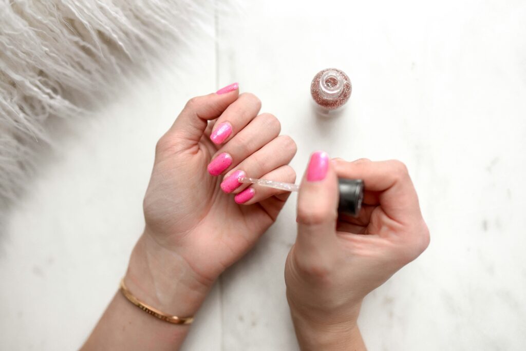 A close-up of a woman painting her fingernails with gel polish at home, with nail products visible in the background—illustrating DIY manicure practices and potential gel manicure allergy risks.

