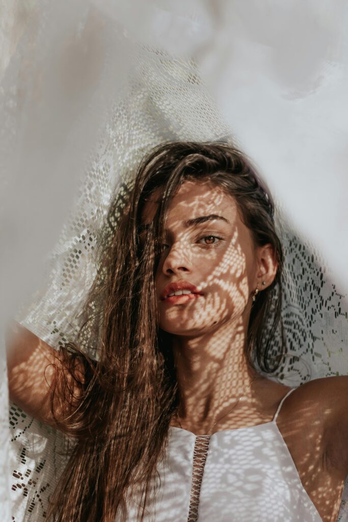 A thoughtful model looking into a mirror, her expression showing concern as she examines tight, dehydrated skin around her eyes and mouth.